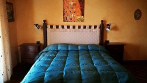 A bedroom with a blue quilted bedspread, a wooden headboard, two bedside tables, and a painting on the wall. - Villa Agreste (Cupello)
