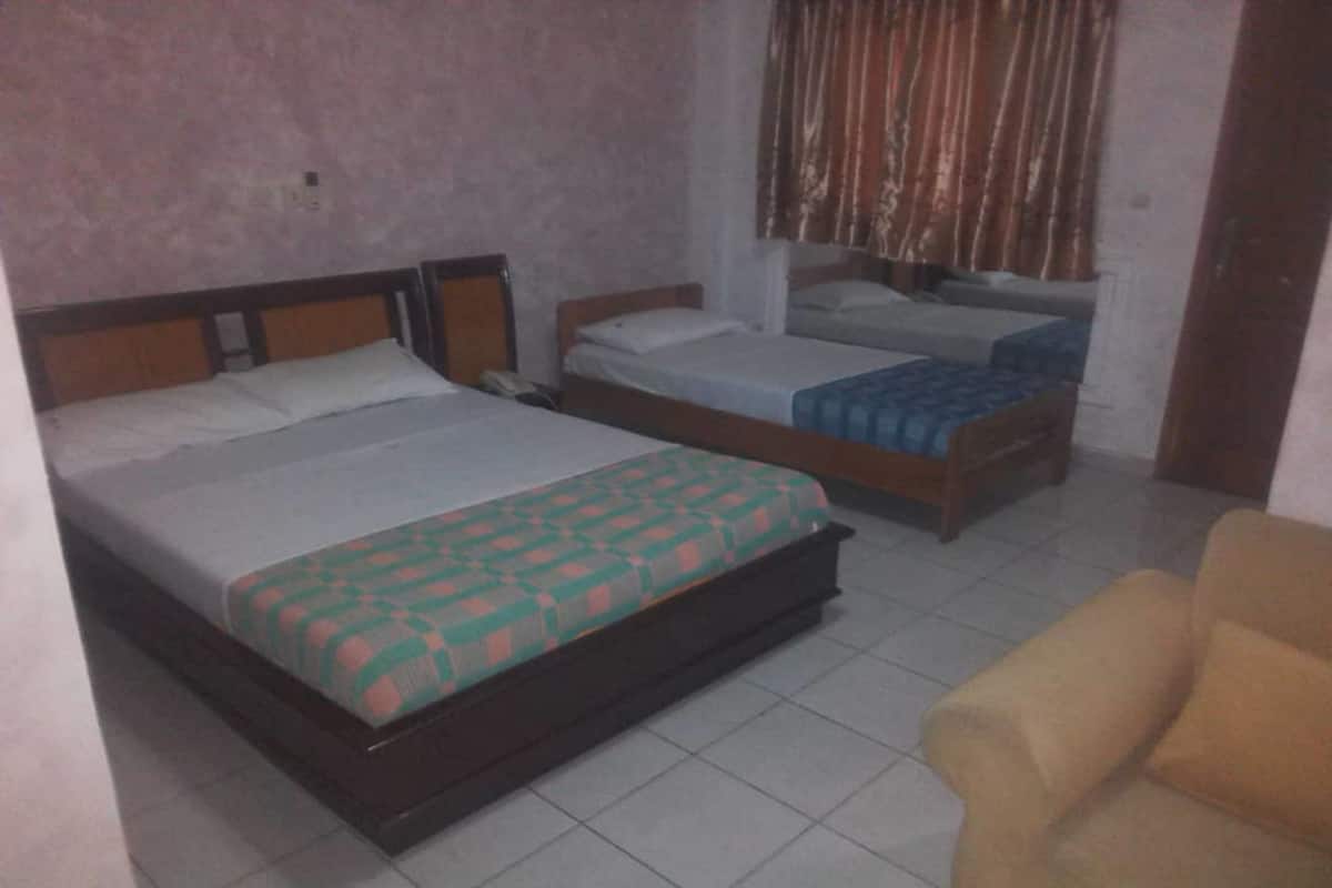 A room with a large bed, two smaller beds, a chair, and a window with curtains.