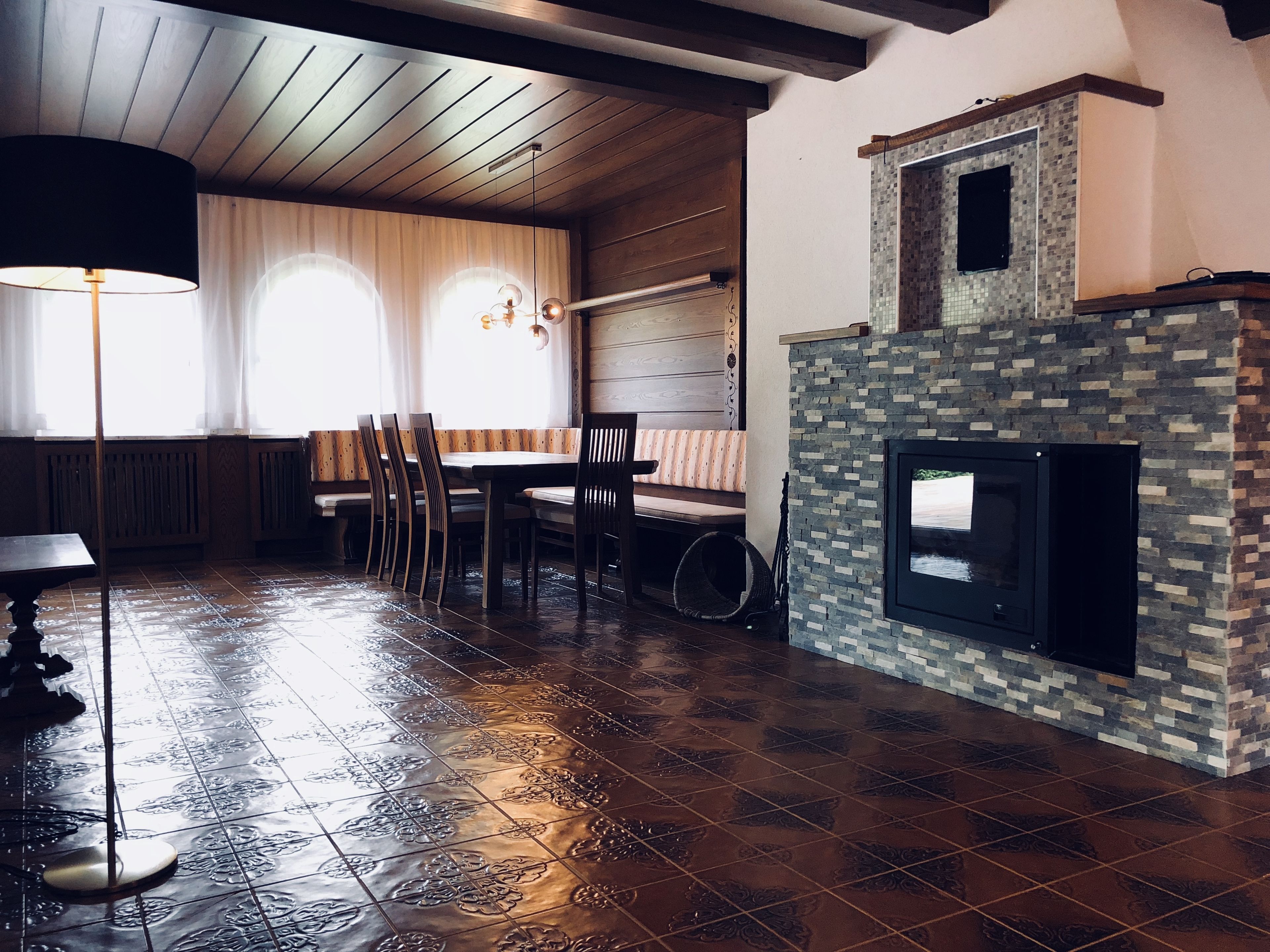 Un coin repas chaleureux avec une table et des chaises en bois, un banc et une cheminée ornée de mosaïques.