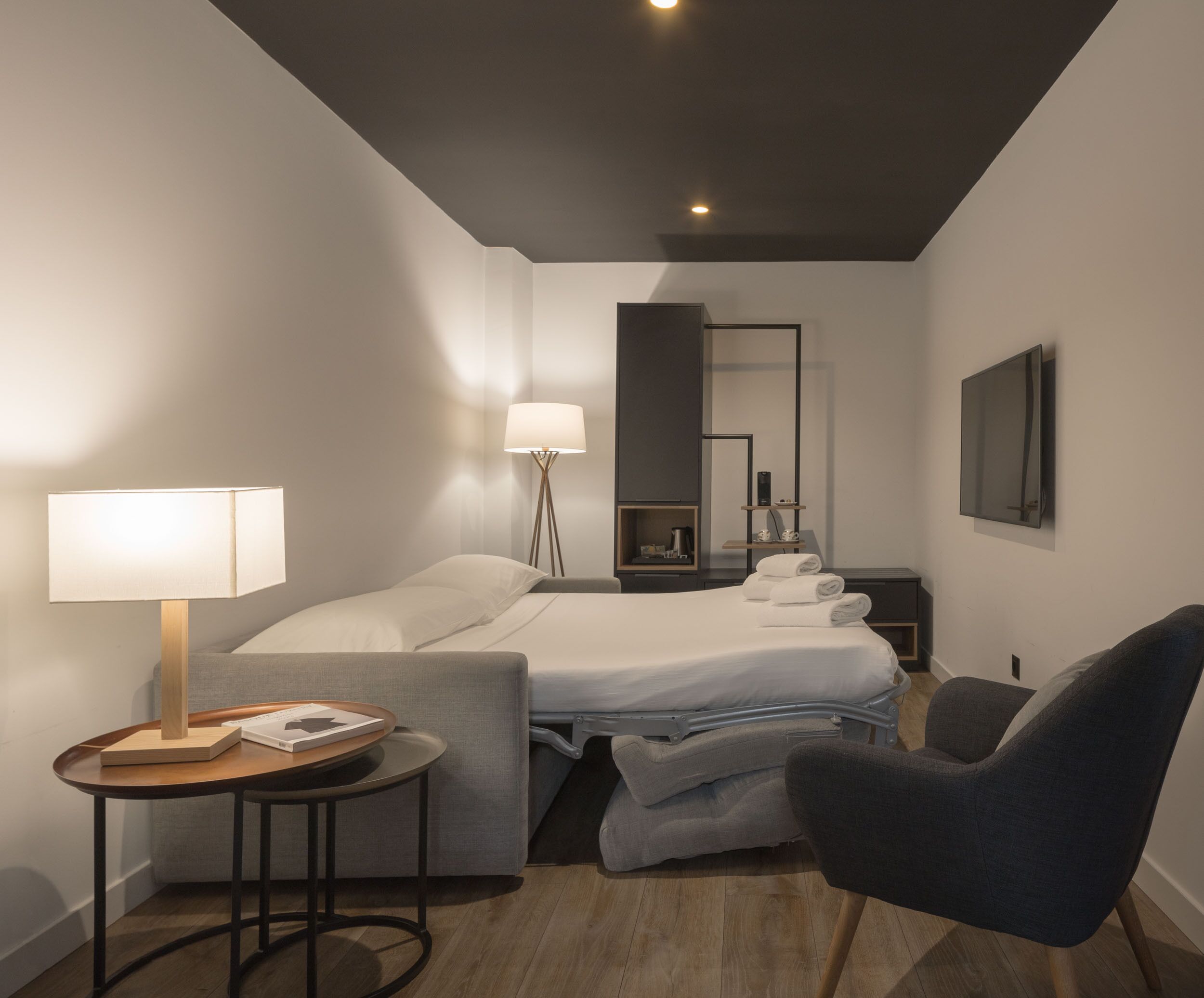 A modern hotel room with a bed, bedside table, lamp, chair, and a mirror.