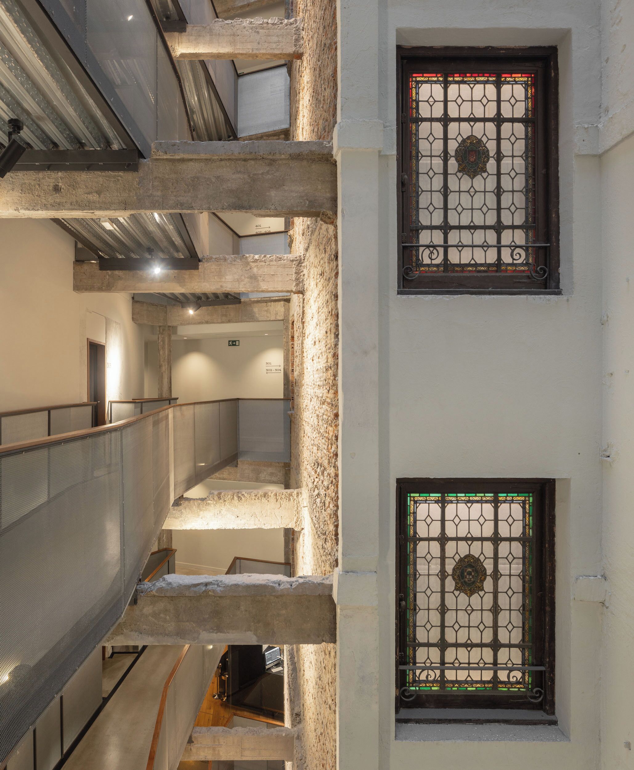 Een meerlaags interieur met zichtbare betonnen balken, metalen leuningen en decoratieve glas-in-loodramen.