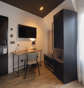 Une chambre moderne et compacte, dotée d’un bureau en bois, d’une chaise, d’un téléviseur à écran plat fixé au mur, d’une petite table avec une lampe et d’une bibliothèque intégrée.