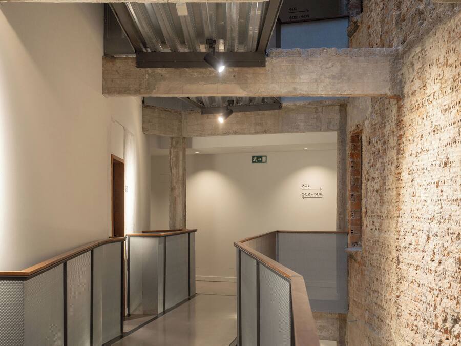 Un pasillo con techo alto, paredes de ladrillo visto y una escalera de metal.