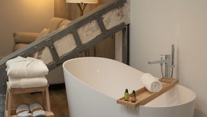 Un baño moderno con una bañera independiente, un taburete de madera con toallas y un estante pequeño con artículos de aseo.