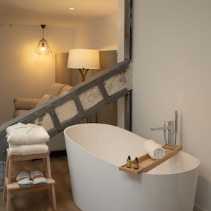 Une salle de bain moderne avec une baignoire sur pieds, un tabouret en bois avec des serviettes et une petite étagère contenant des articles de toilette.