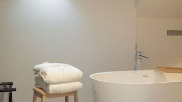 A bathroom with a freestanding bathtub, a wooden stool with towels, and a window with natural light.