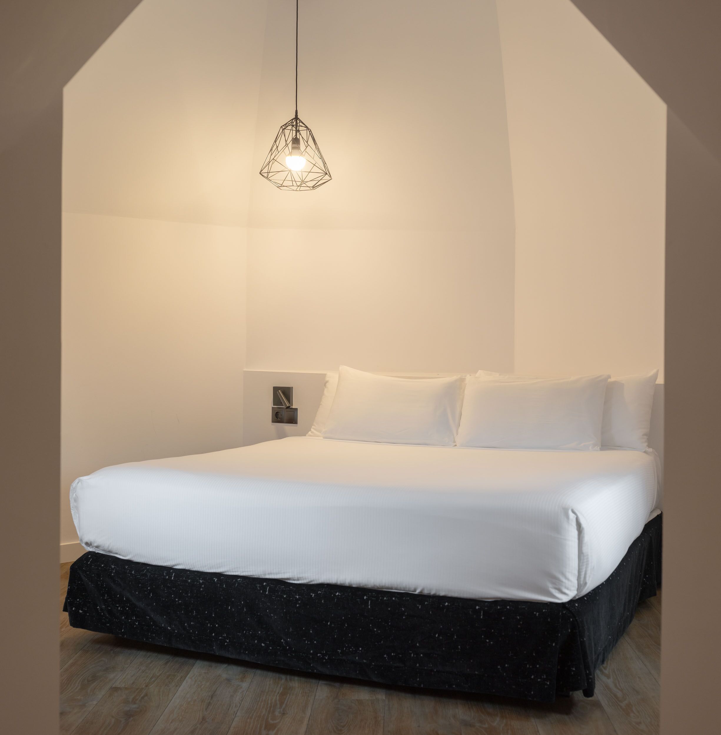 Un dormitorio moderno con una cama grande, una lámpara colgante geométrica y suelo de madera.