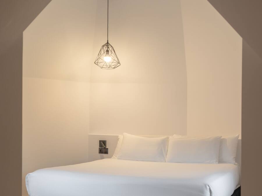 Un dormitorio moderno con una cama grande, una lámpara colgante geométrica y suelo de madera.