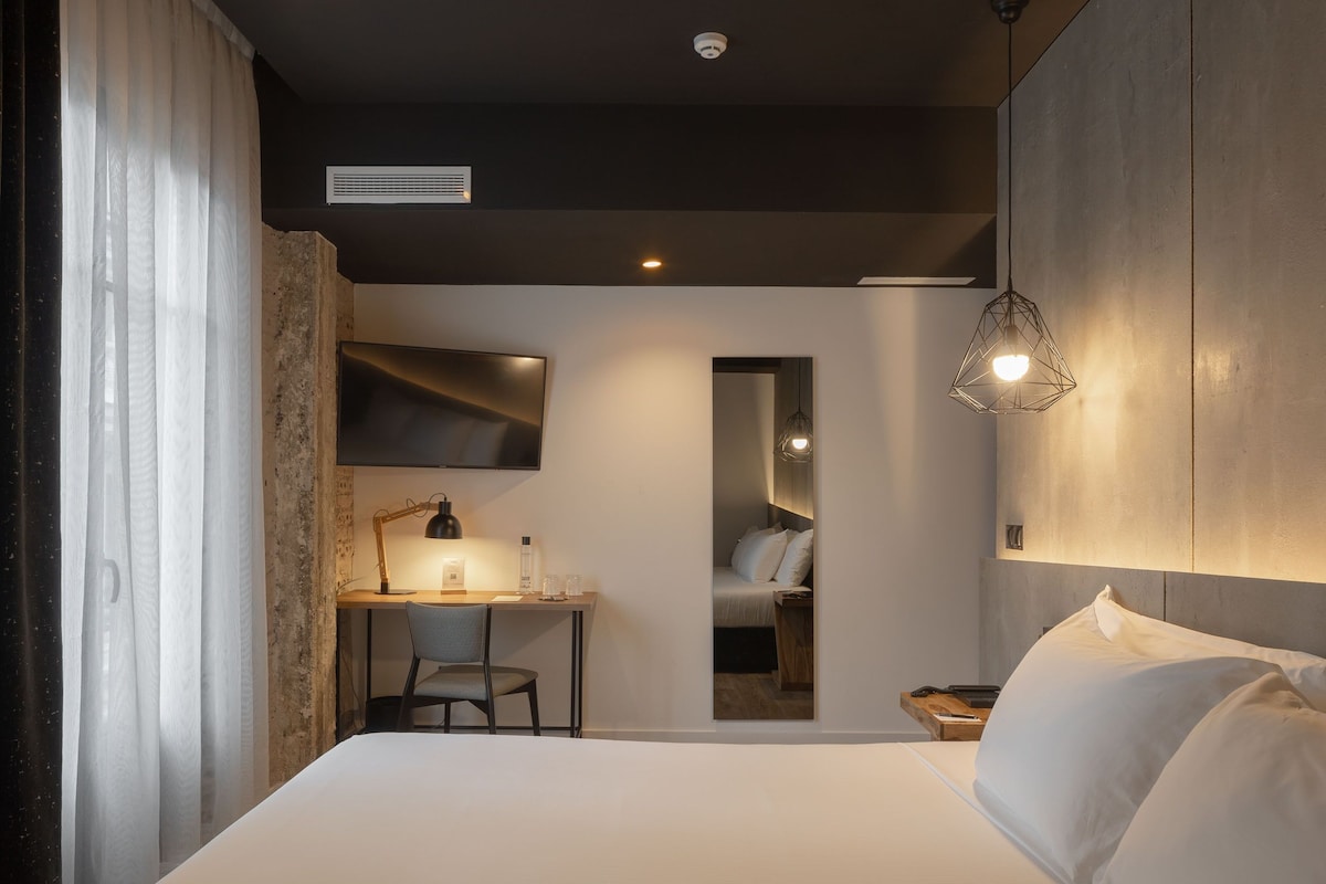 Une chambre moderne avec un grand lit, un bureau avec une chaise, une télévision et un luminaire suspendu.