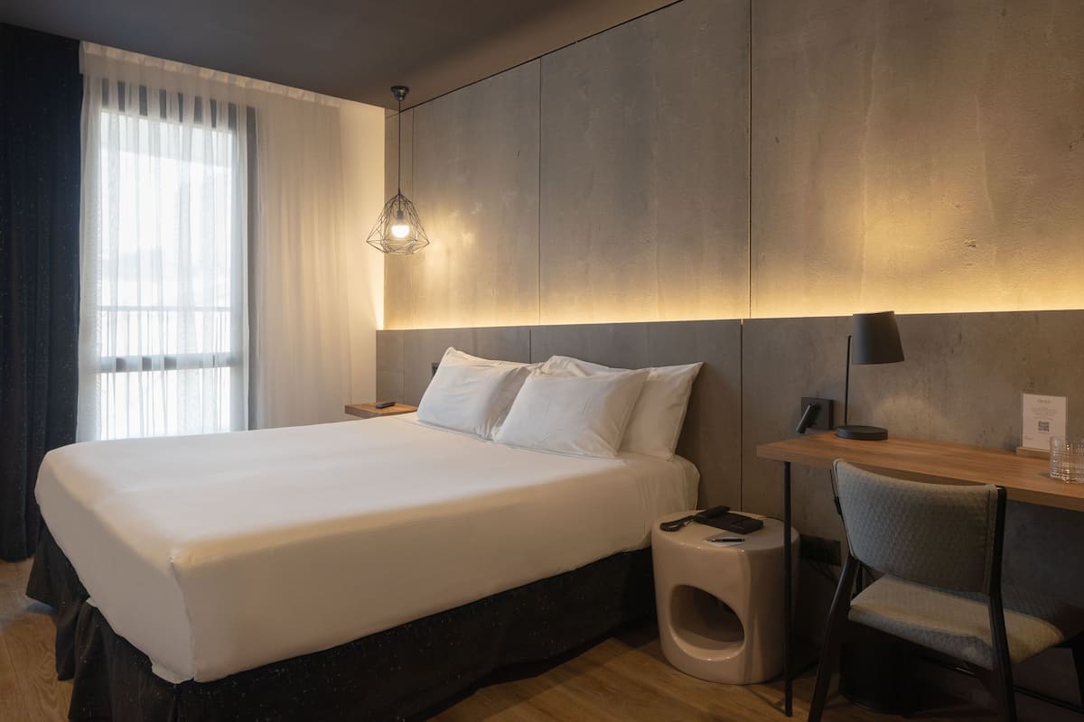 A modern hotel room with a large bed, a desk, and a chair.