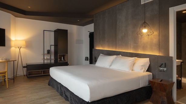 Un dormitorio moderno con una cama grande, una mesita de noche, una lámpara de pie, un espejo y un armario.