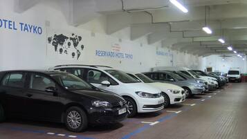 A row of parked cars in a hotel parking garage with signs indicating reserved parking for Hotel Tayko.