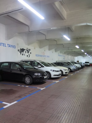 Une rangée de voitures garées dans le parking souterrain d’un hôtel, avec des panneaux indiquant des places de stationnement réservées à la clientèle de l’hôtel Tayko.