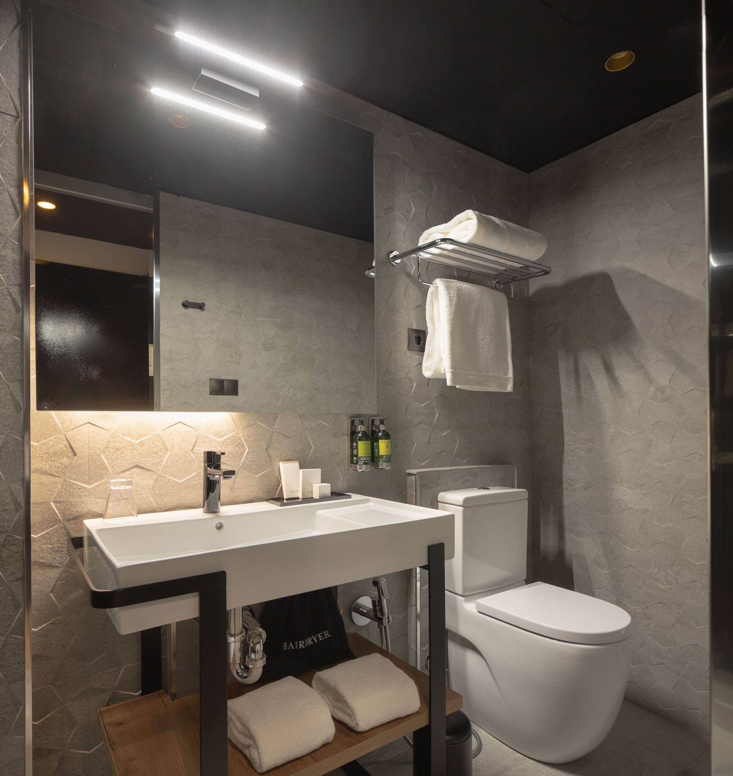 A modern bathroom with a large mirror, a white sink, a toilet, and a towel rack.