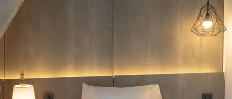 A modern bedroom with a large bed, a bedside table with a lamp, and a geometric pendant light.