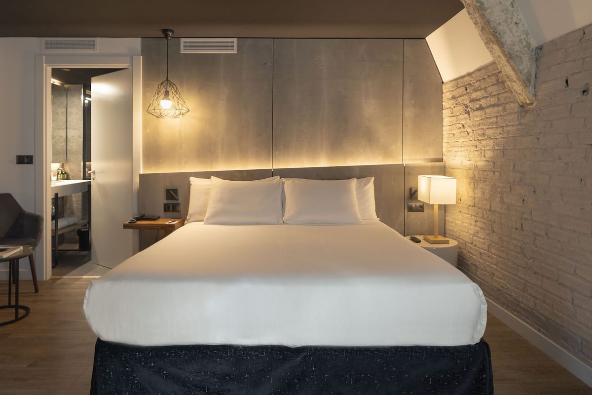 A modern hotel room with a large bed, a desk, and a chair.