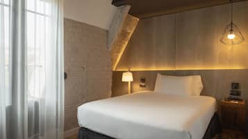 A modern bedroom with a large bed, a wooden headboard, a sloped ceiling, and a hanging light fixture.