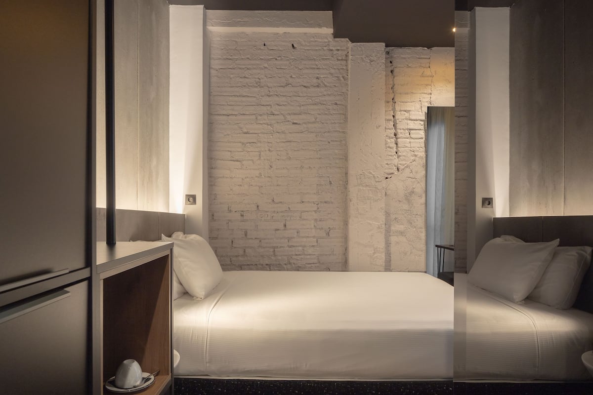 A modern bedroom with a brick wall, a bed with white bedding, and a wooden nightstand.