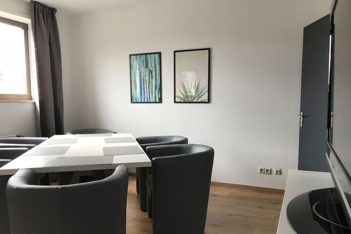 Une chambre d’hôtel moderne avec un grand lit, un bureau équipé d’un ordinateur et un téléviseur. Deux œuvres d’art encadrées ornent le mur, et une fenêtre est agrémentée de rideaux.