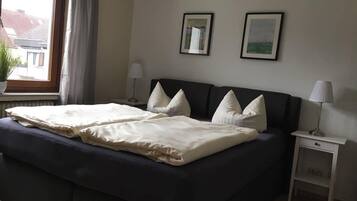 A neatly made bed with white linens and pillows, a bedside table with a lamp, and two framed pictures on the wall.