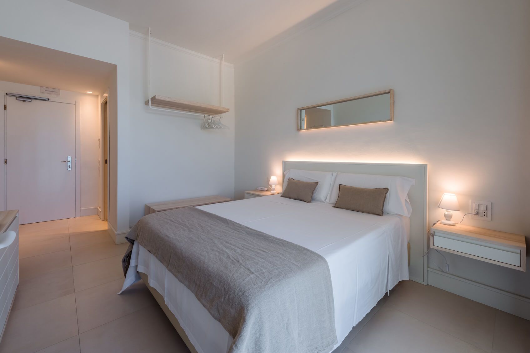 A neatly arranged bedroom with a large bed, bedside tables, a mirror, and a wardrobe.
