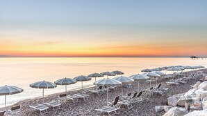 A beach with rows of sun loungers and umbrellas, a calm sea, and a pier in the distance. - Hotel La Chiave dei Trabocchi (San Vito Chietino)