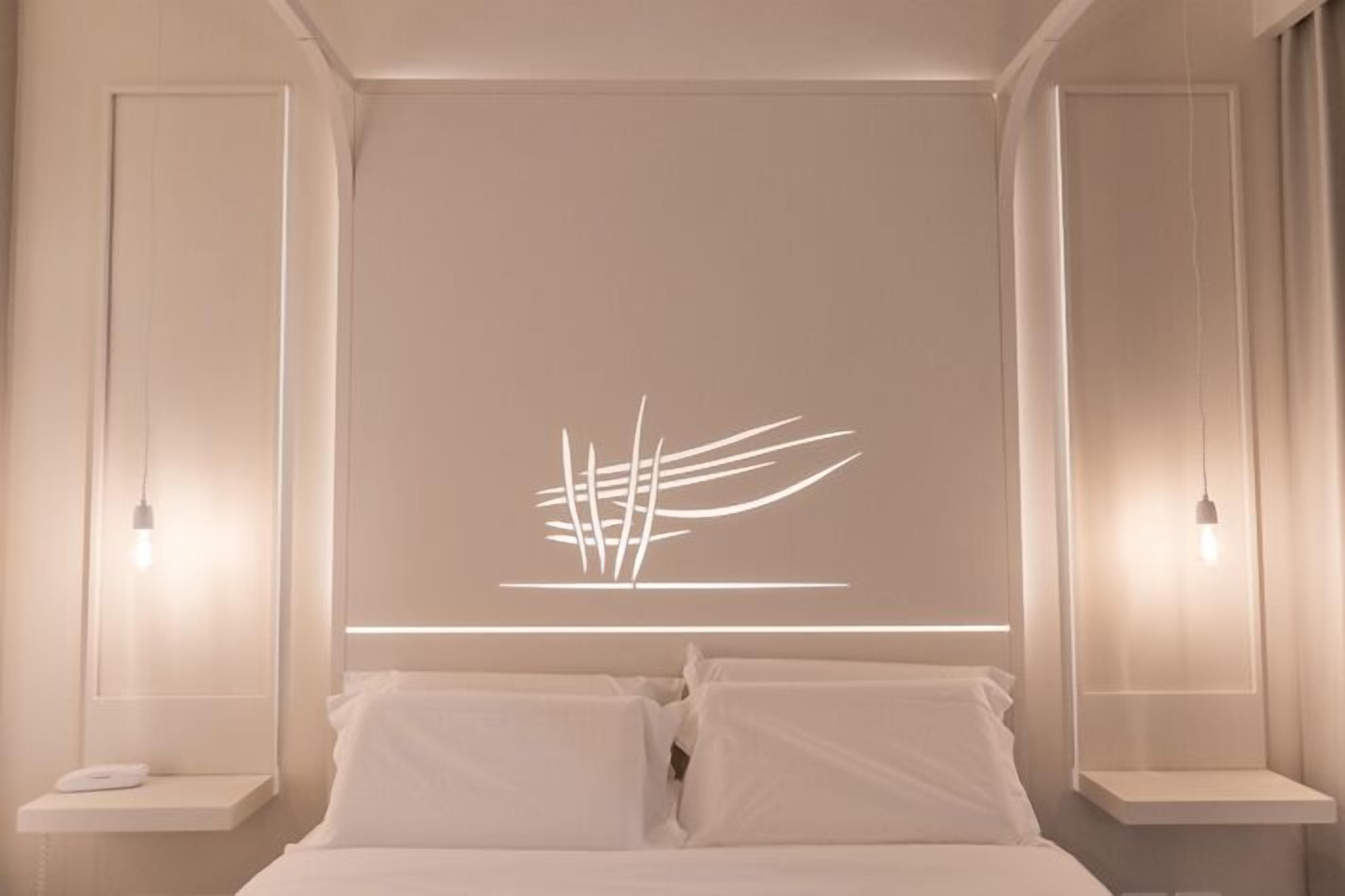 Quarto moderno com cama posicionada sob uma luminária fixada na parede.