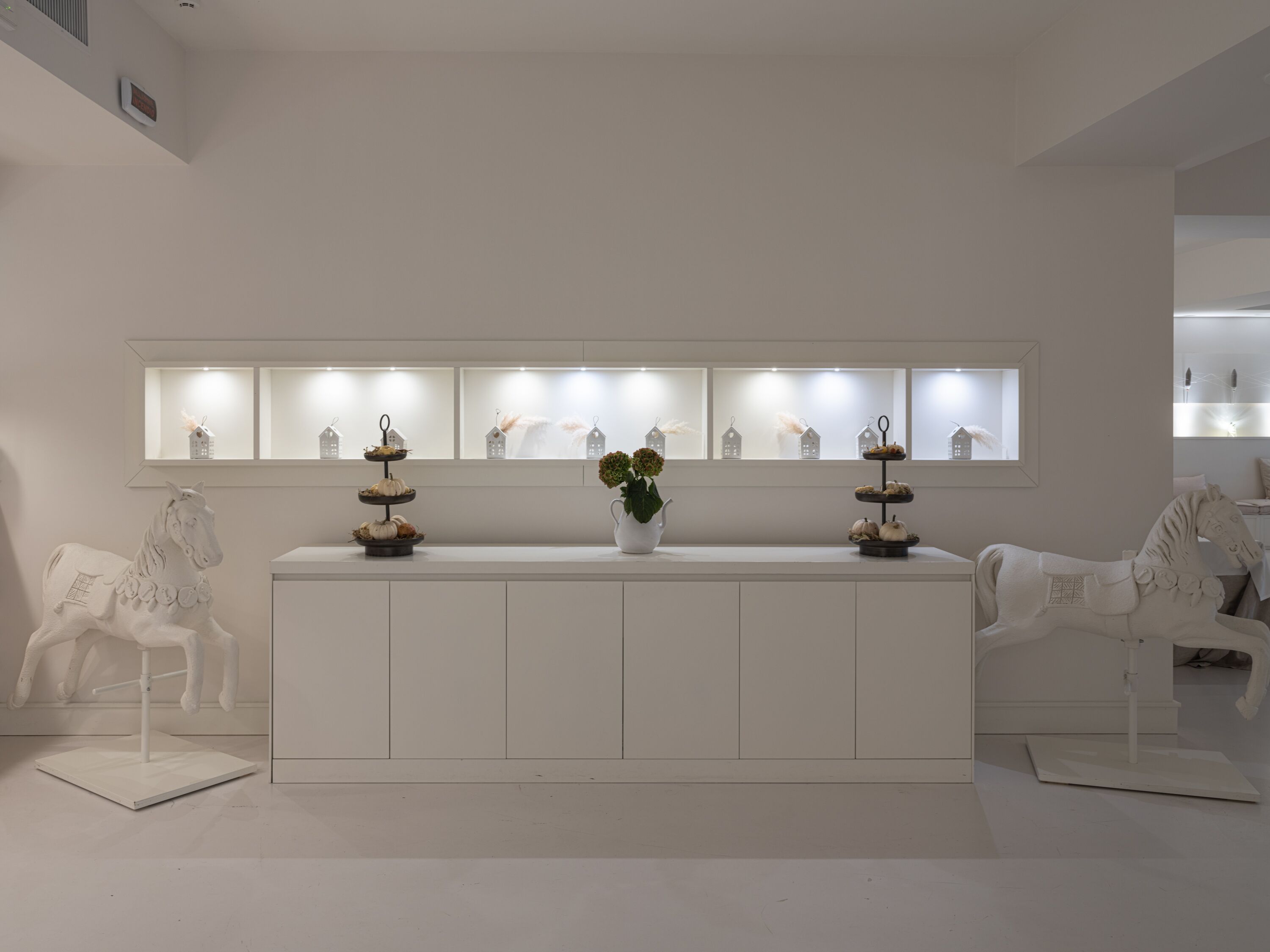 A minimalist white reception desk with a tiered display of pastries and a vase of flowers.