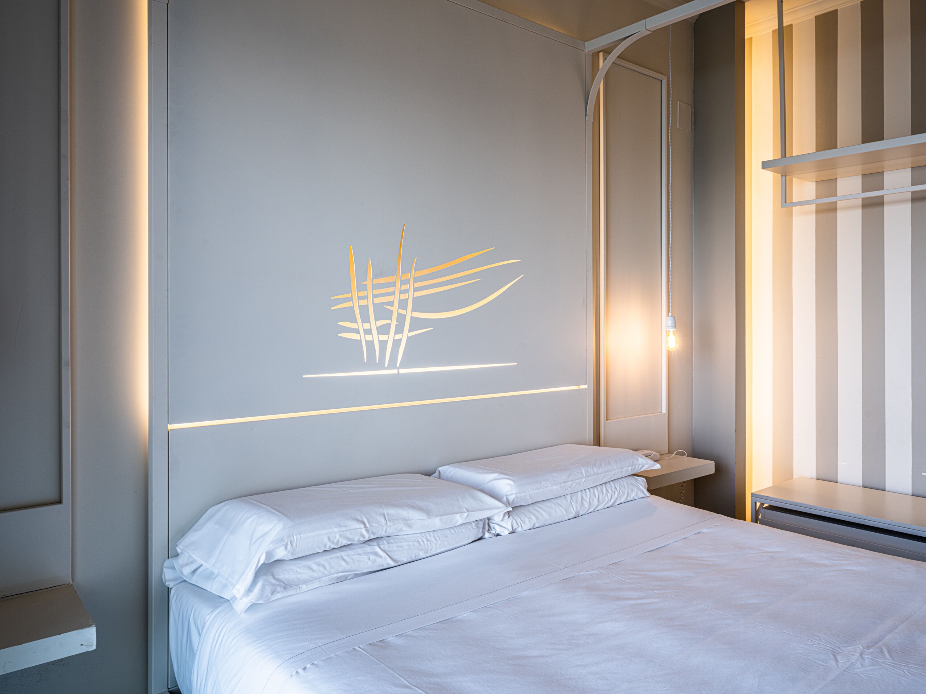 Habitación de hotel moderna con una cama bien hecha, una mesita de noche y una lámpara fijada a la pared.