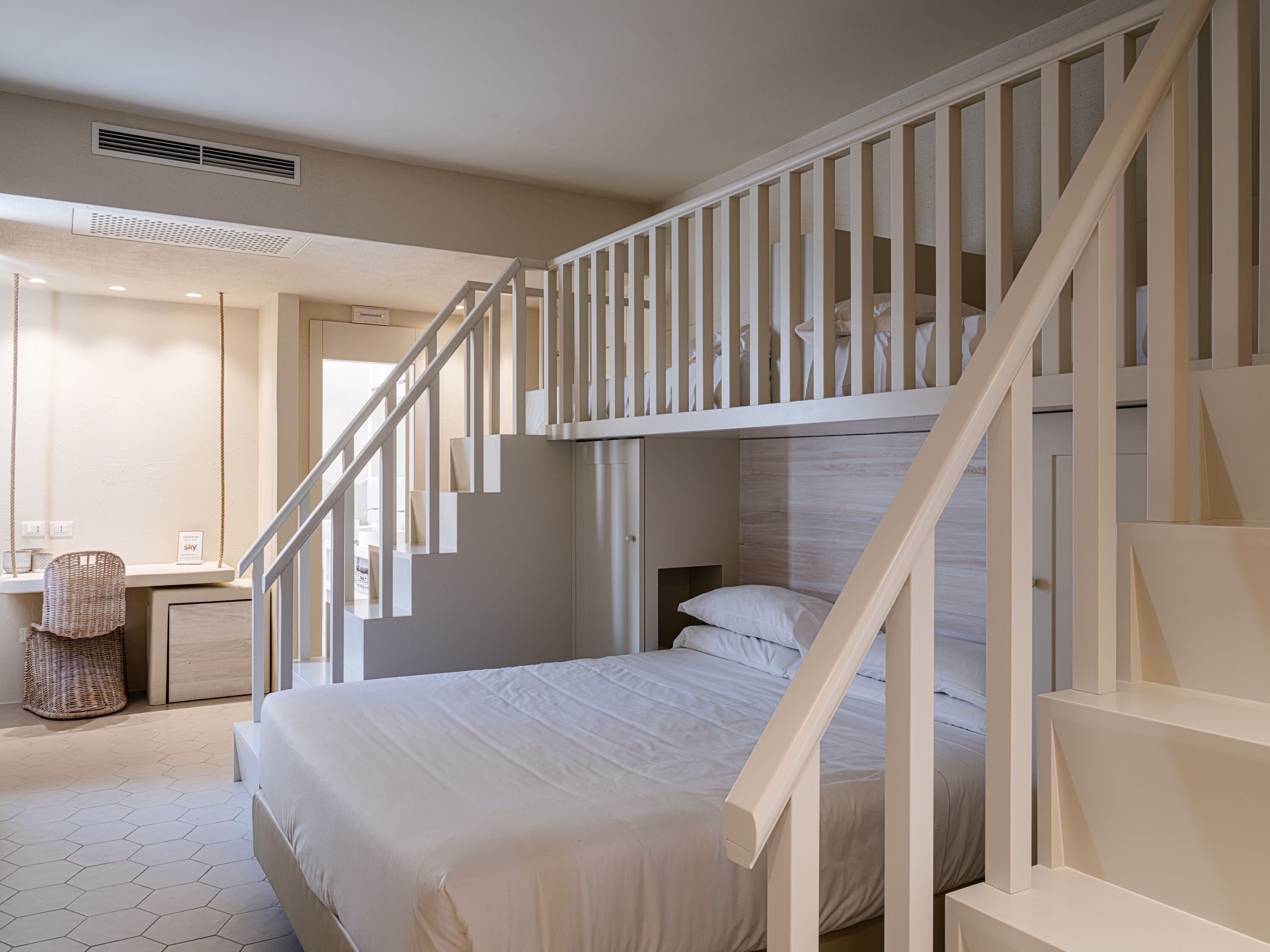A bedroom with a bunk bed, a desk with a chair, and a hanging basket.