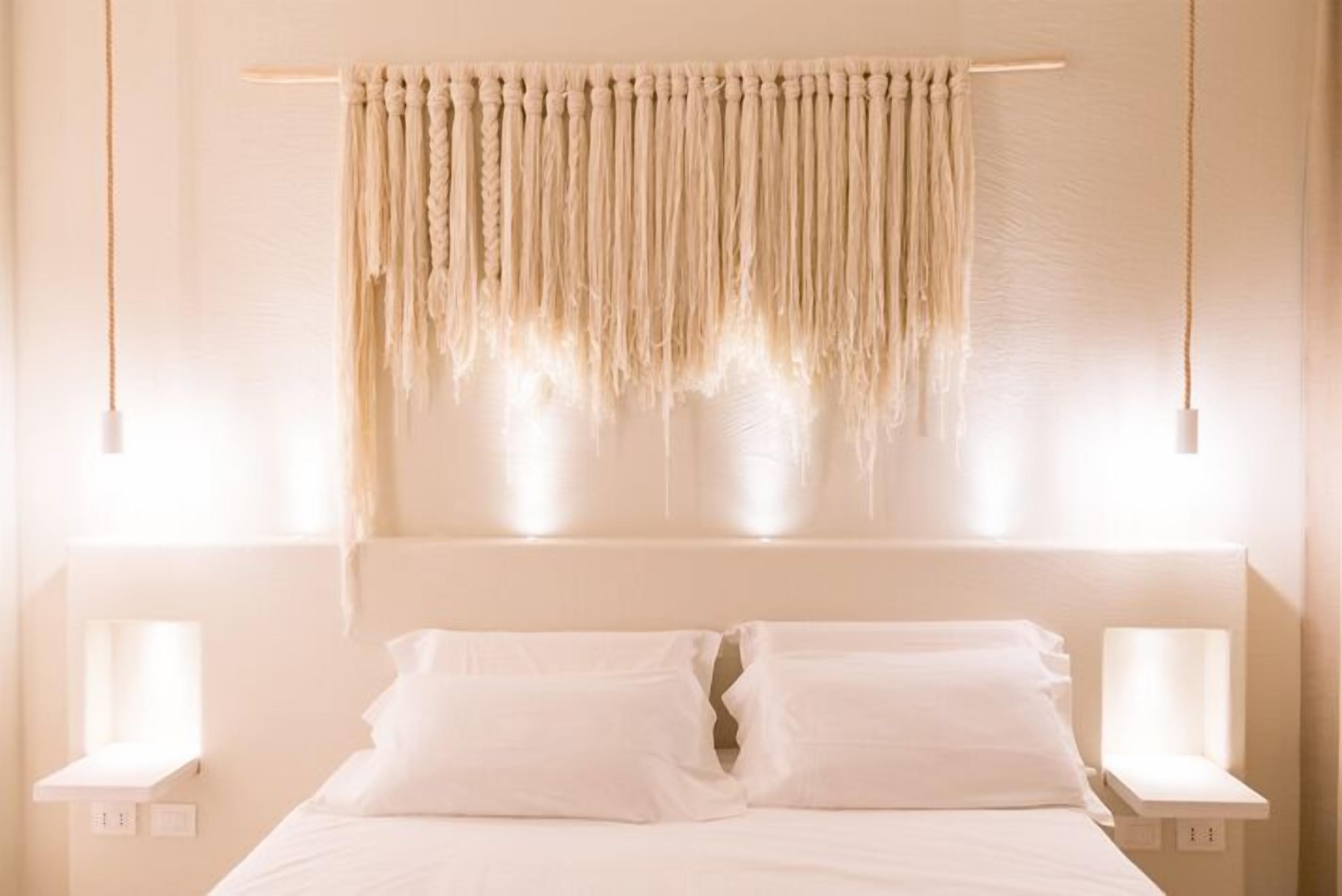 A bed with white linens and a headboard, two bedside tables with lamps, and a macramé curtain.