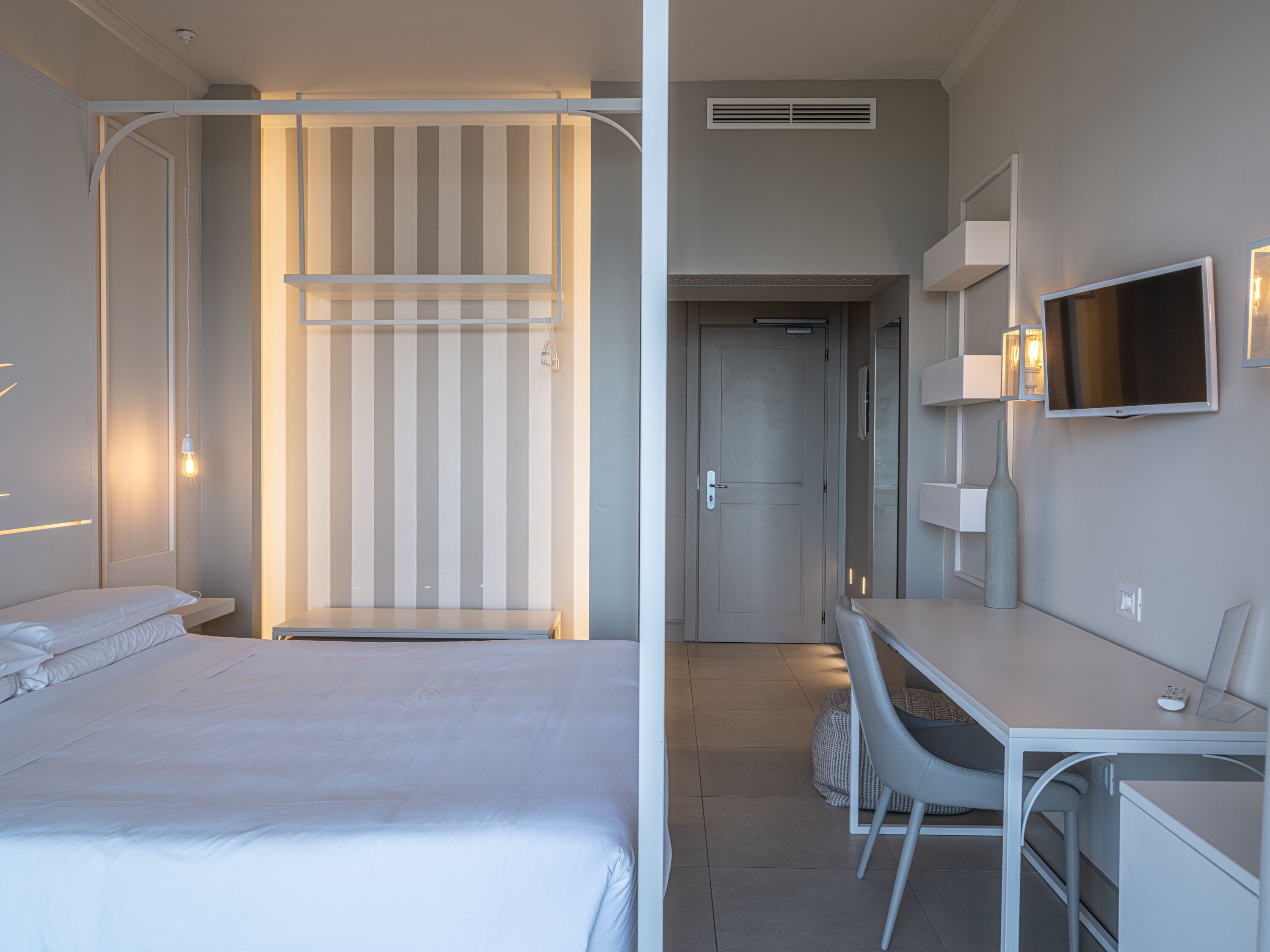 Una camera d'albergo con un letto, una scrivania, una sedia, una televisione e un armadio.