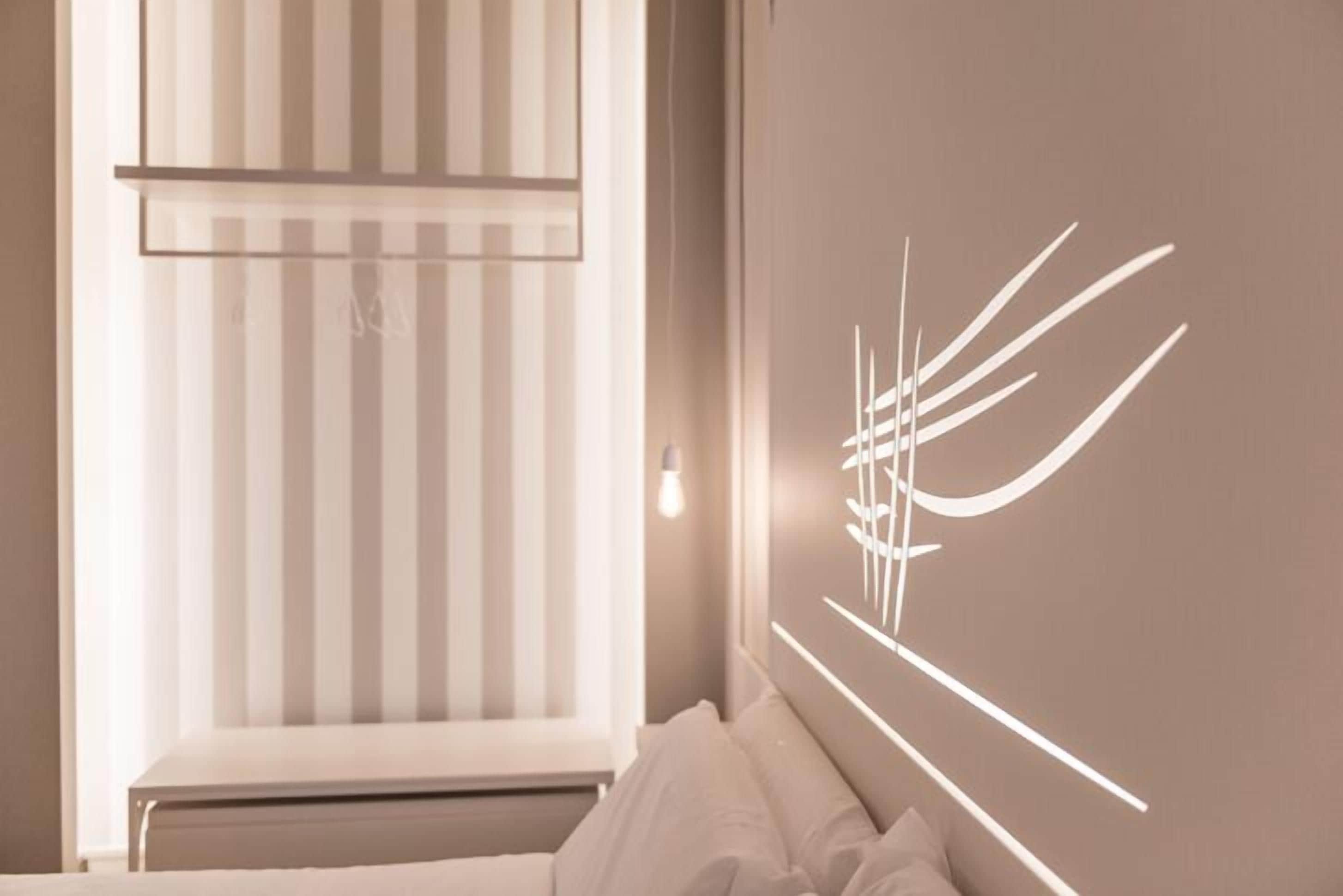 Un dormitorio con cama, ventana con persianas y una lámpara de pared.