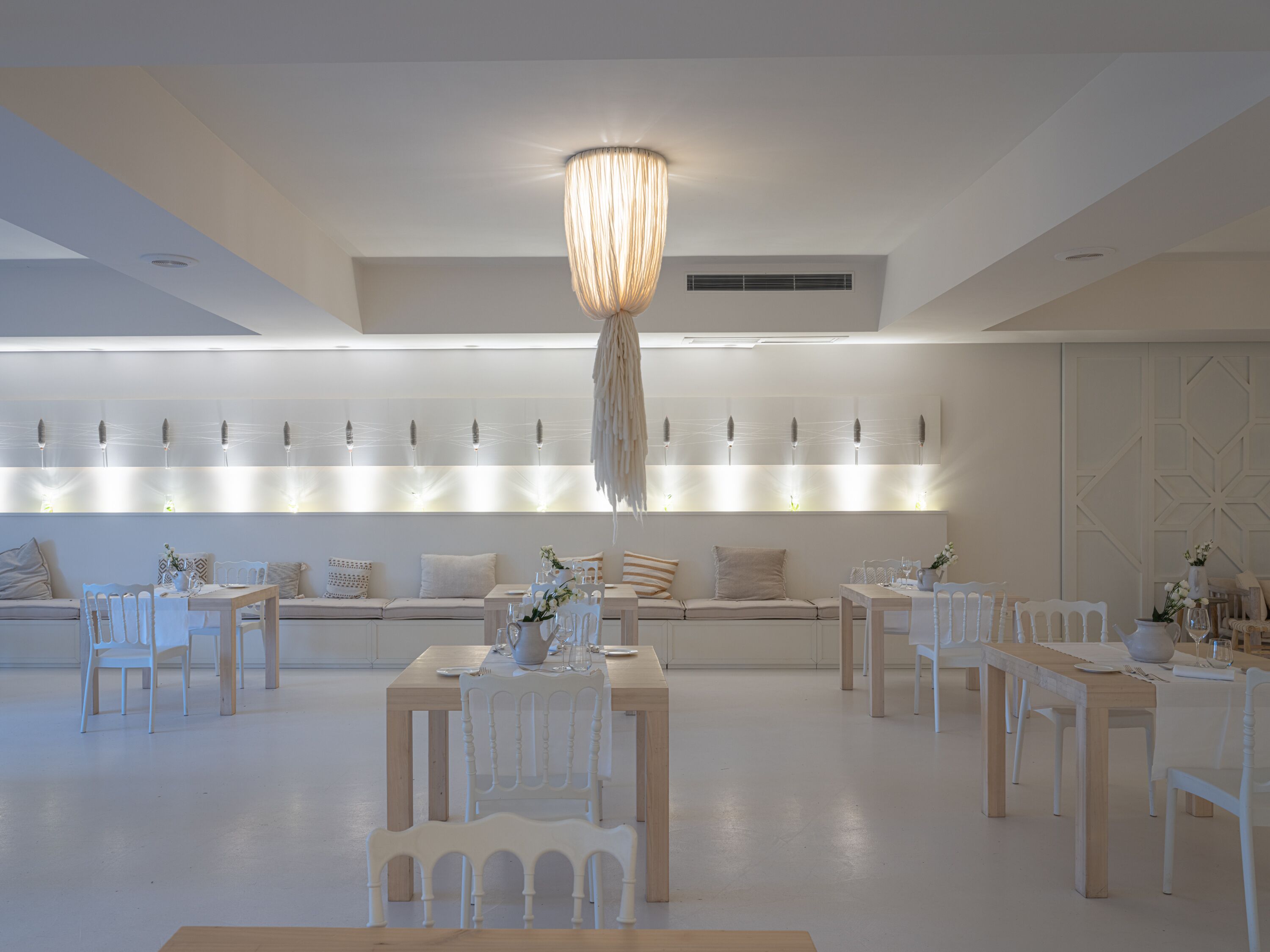 Un comedor moderno con mobiliario blanco, una lámpara central y una exhibición de luces en la pared.