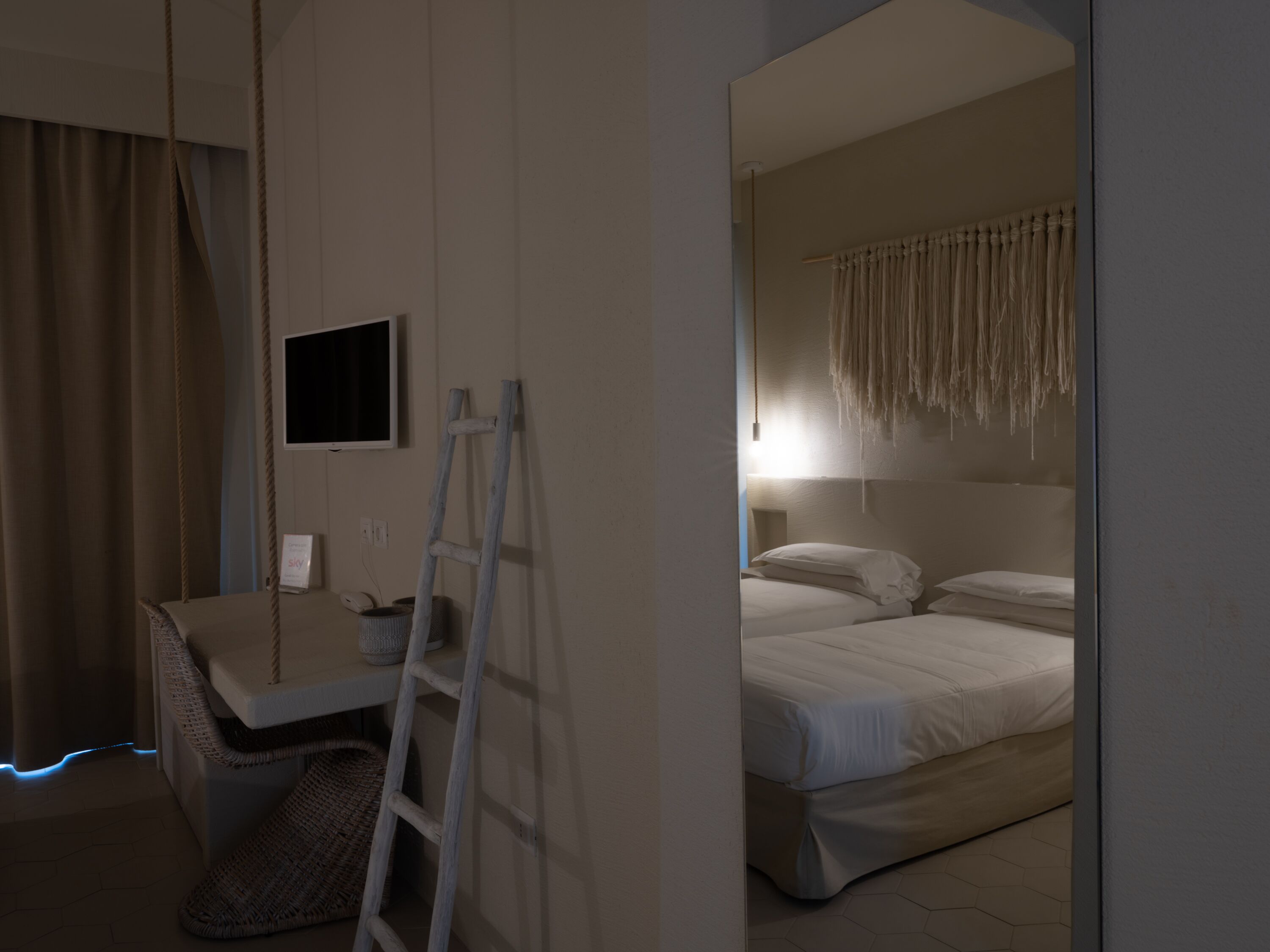 A bedroom with a bed, a desk, a chair, a TV, and a ladder.