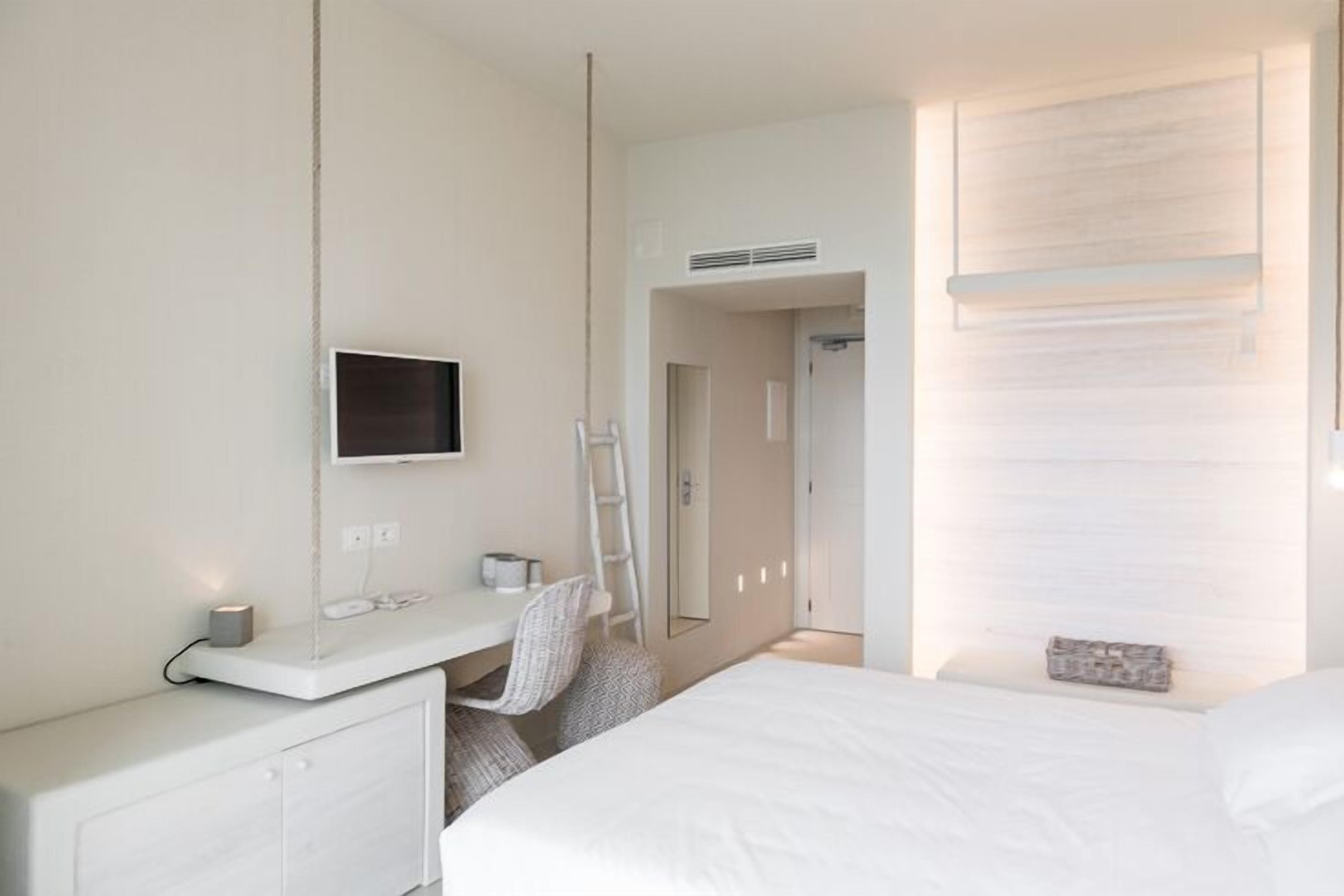 Habitación de hotel con cama, escritorio con silla, televisor y armario.