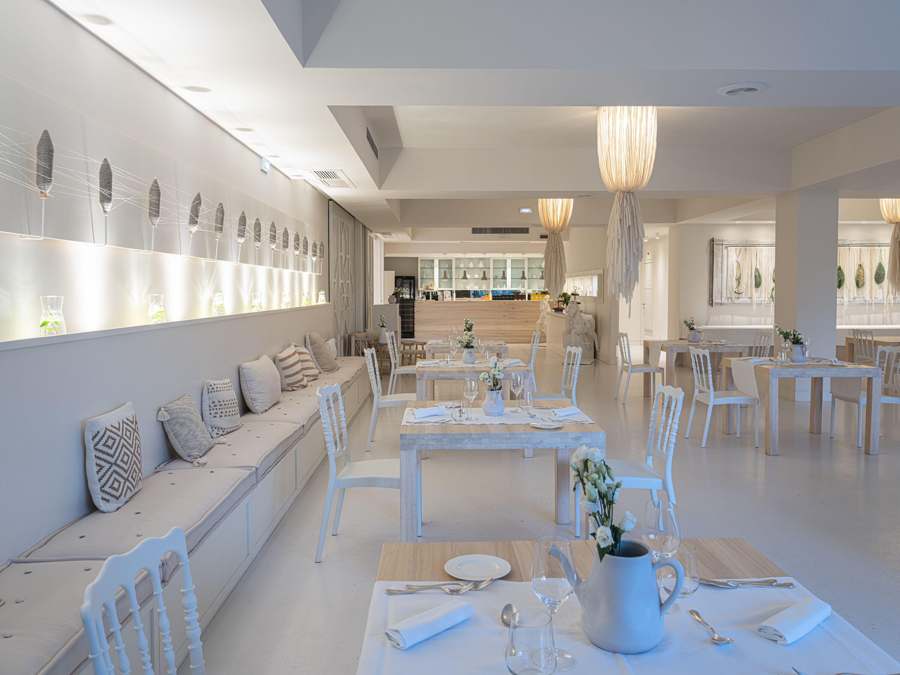 Un'area pranzo moderna con arredi bianchi, una zona salotto centrale e un bar sullo sfondo.