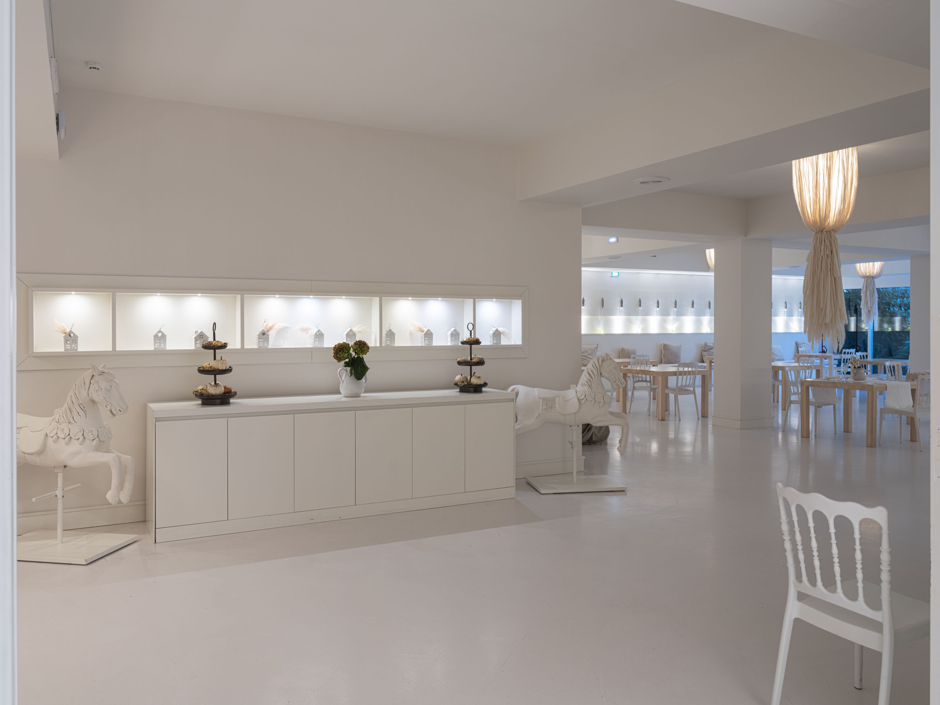 Un vestíbulo de hotel moderno y minimalista con un mostrador de recepción central, muebles blancos y vistas al área de comedor.