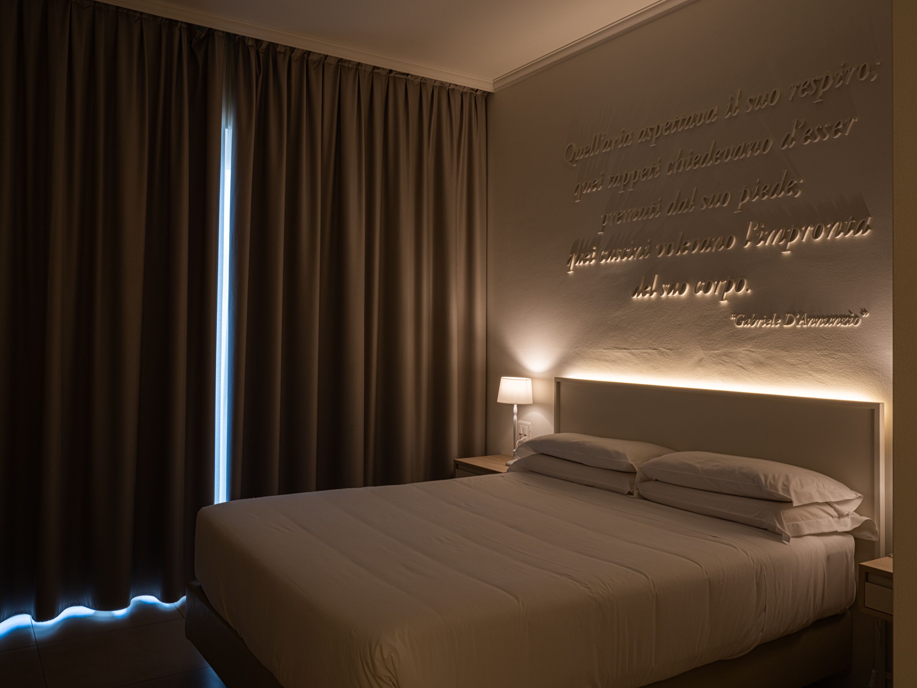 A hotel room with a large bed, a nightstand with a lamp, and a wall with an inspirational quote.