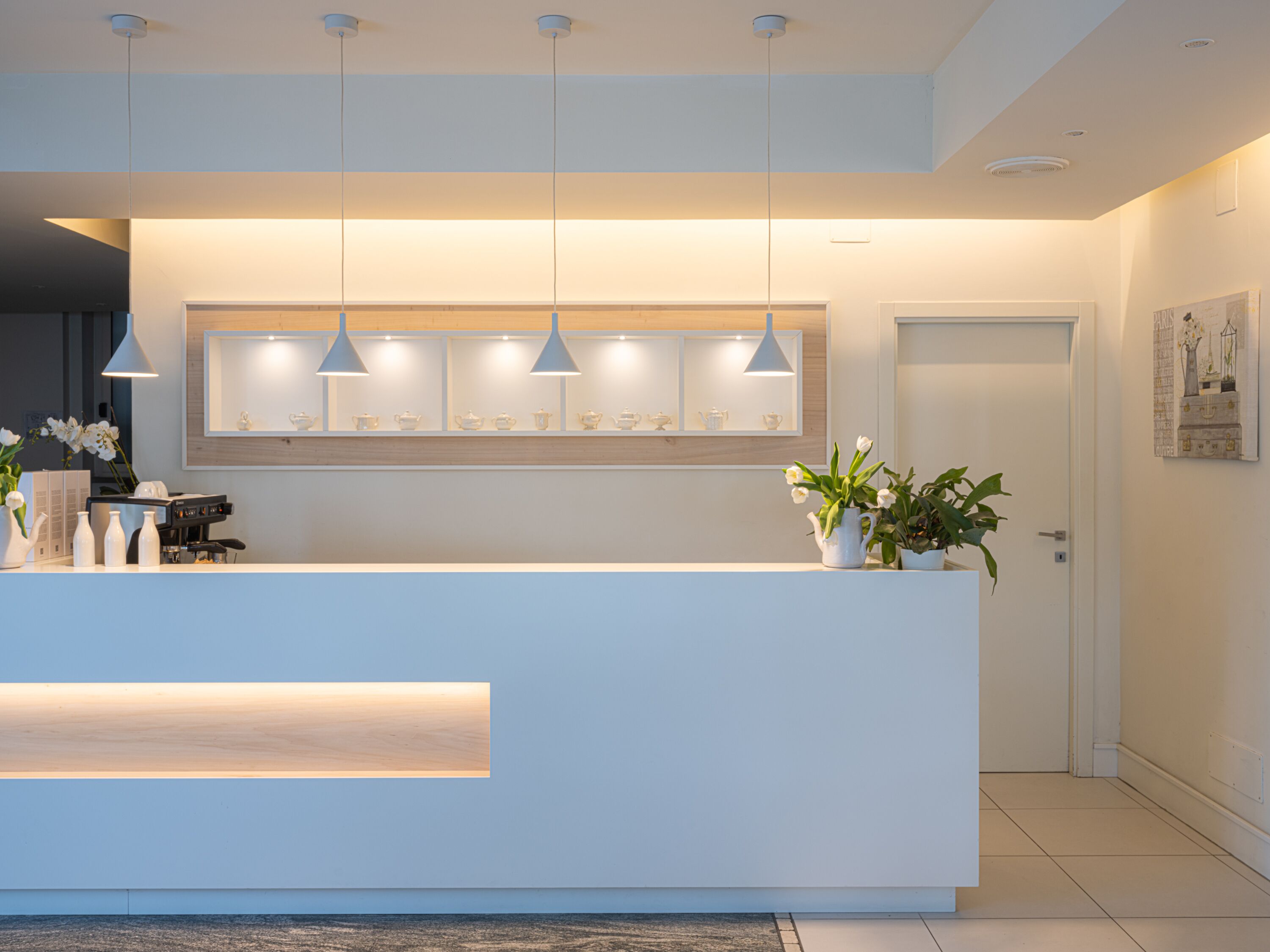 A modern reception desk with pendant lighting, a wooden panel above, and a door to the right.