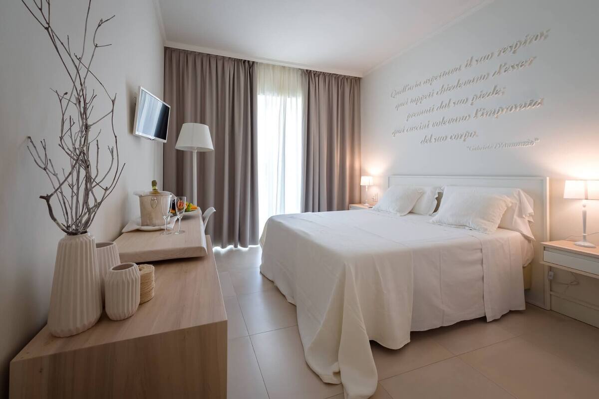 Ein modernes Hotelzimmer mit einem großen Bett, einem Flachbildfernseher, einem Schreibtisch mit Lampe und einem dekorativen Zweig auf der linken Seite.