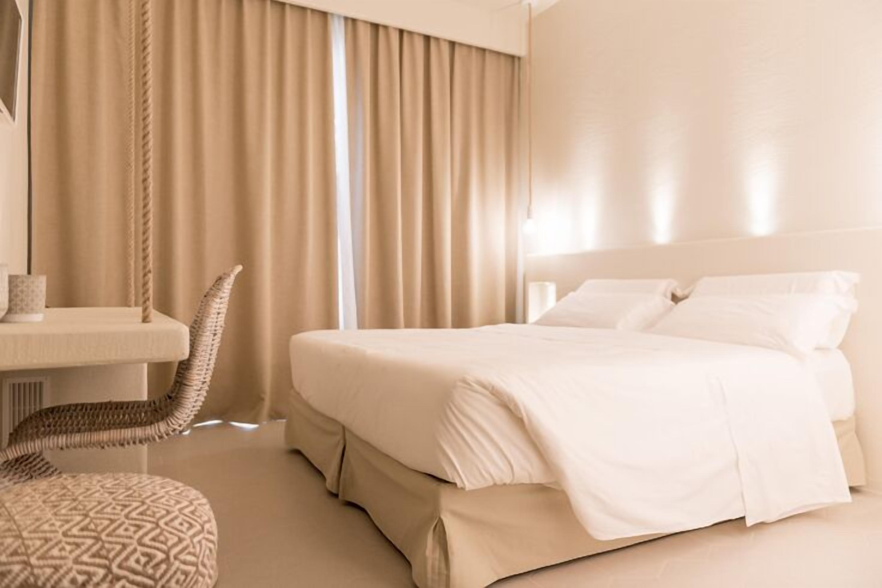 Una camera d'albergo con un letto, una sedia, un tavolino e una tenda.