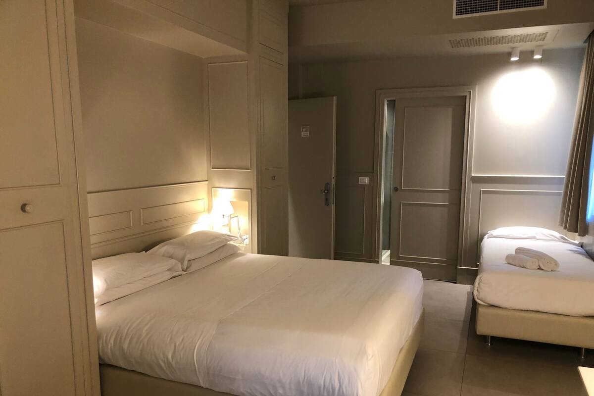 Ein Hotelzimmer mit einem großen Bett, einem kleineren Bett, einem Kleiderschrank und einer Tür.