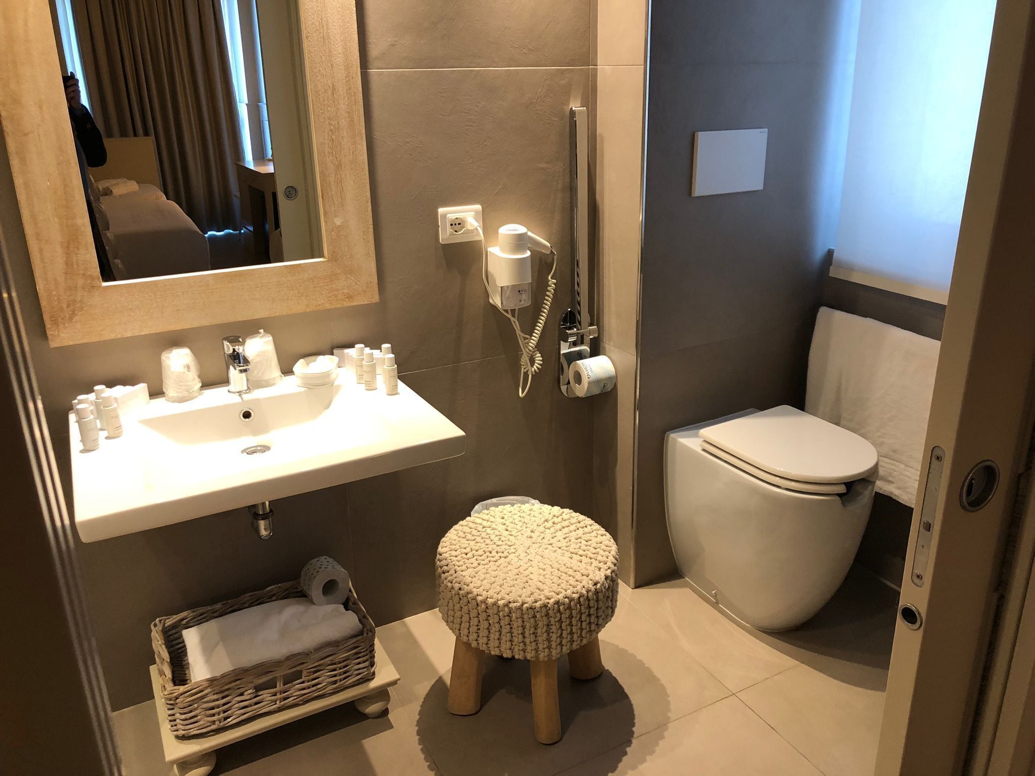 Ein modernes Badezimmer mit Waschbecken, Spiegel, Toilette und einem kleinen Hocker.