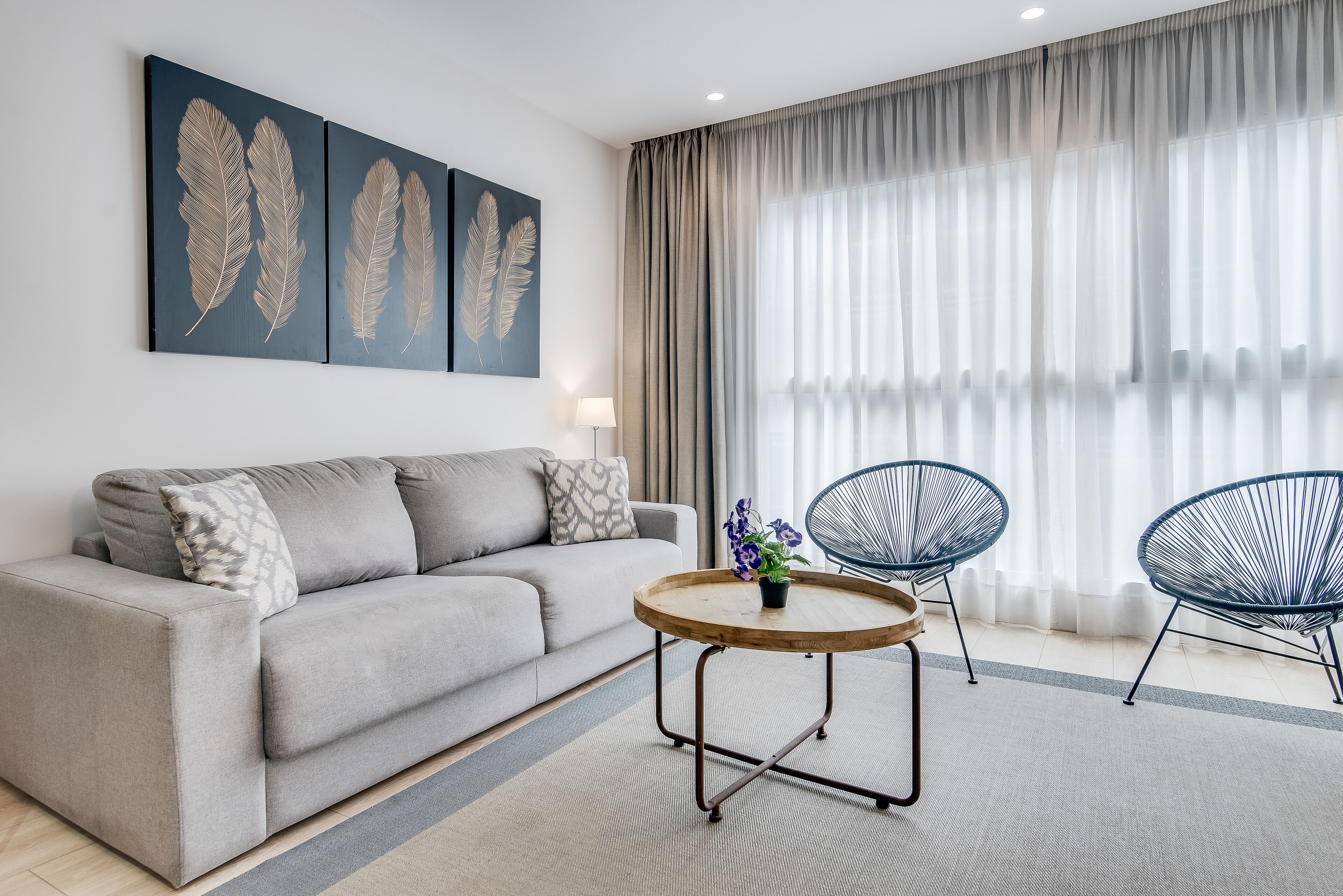 A modern living room with a grey sofa, two armchairs, a round coffee table with a plant, and artwork on the wall.