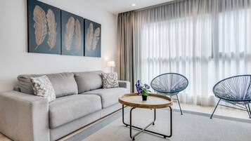 A modern living room with a grey sofa, two armchairs, a round coffee table with a plant, and artwork on the wall.