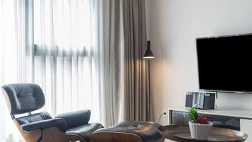 A modern living room with a leather sofa, a small round table with a plant, a floor lamp, and a flat-screen TV mounted on the wall.