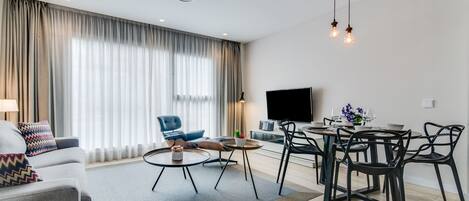 Una sala de estar moderna con sofá, mesa de centro, mesa de comedor y sillas. Un televisor de pantalla plana está montado en la pared.