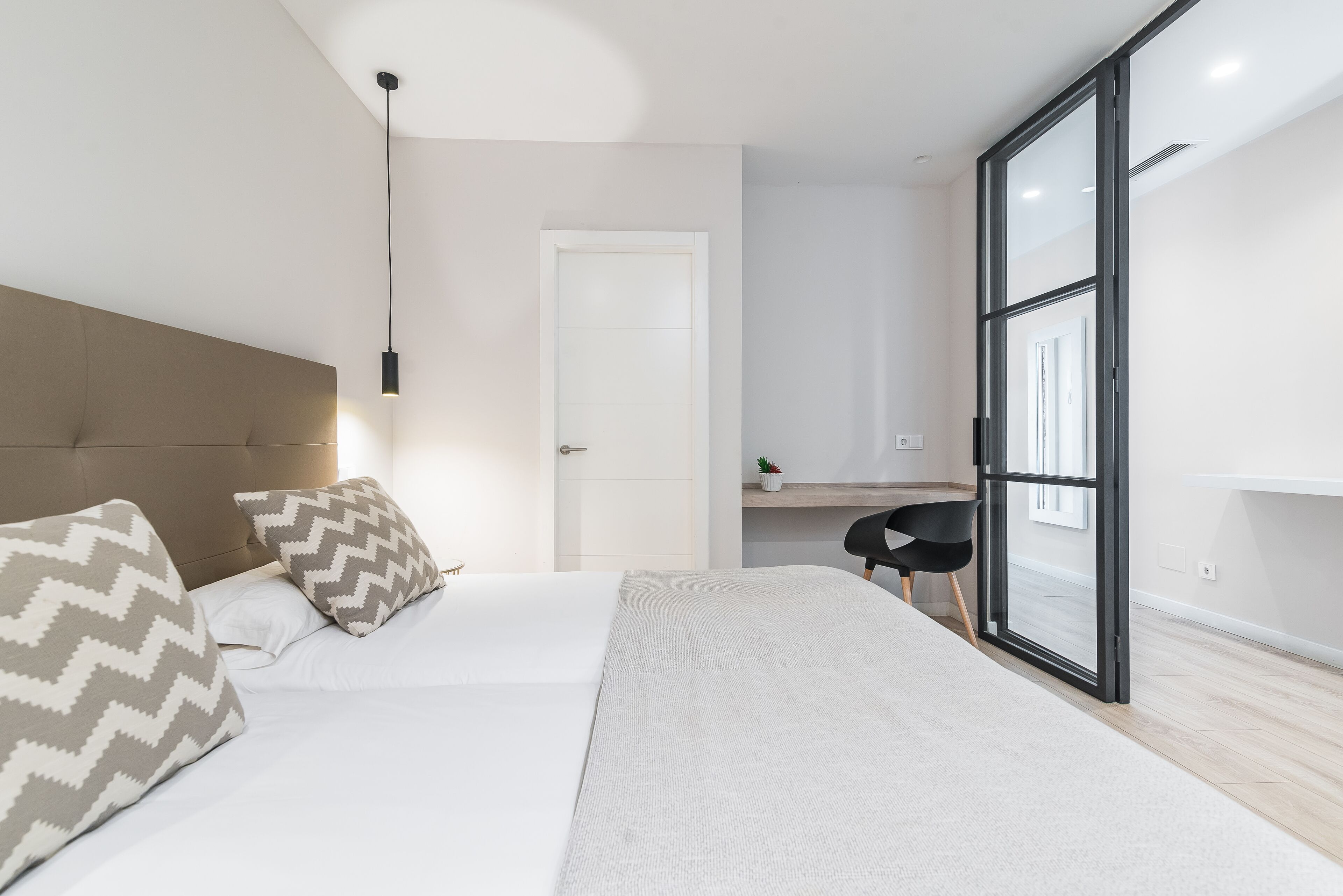 Un dormitorio moderno con una cama grande, un escritorio y un ventanal corredero al exterior.