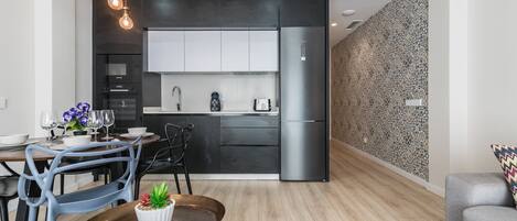 A modern kitchen with a built-in oven, microwave, and refrigerator. There is a dining area with a table and chairs, and a small potted plant on the table.